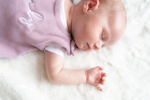 A newborn baby girl asleep on a blanket, with her arm up by her face.