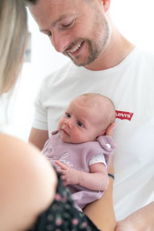 A mum and dad holding their newborn baby girl between them. Taken over the mums shoulder, focusing on the dad and newborn baby.