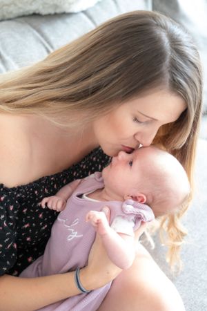 A young mum giving her newborn baby girl a kiss on the cheek.