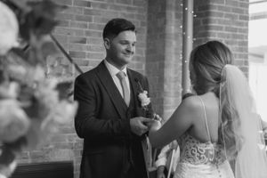 A black and white image of a bride and groom during their wedding ceremony. The focus is on the groom looking at the bride.