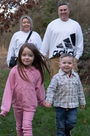 A young family are walking towards the camera. The children are in front, holding hands.