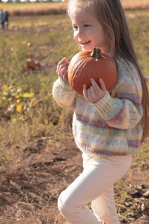 Young girl in a pumpkin field, carrying a pumpkin