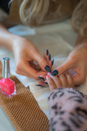 Client getting their nails done, close up, bottle of pink nail varnish.
