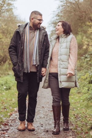Couple holding hands, looking at each other and smiling, walking towards the camera.