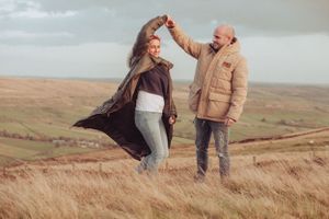 Married couple dancing in the fields, wind is blowing the coat up