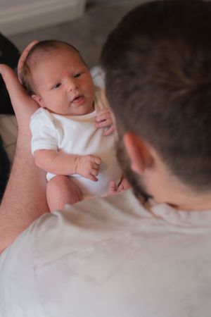 A dad is holding his newborn baby. Photo is taken over dads shoulder and the focus is on the baby.