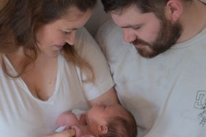 New parents are holding their newborn baby, both looking at the baby with big smiles.