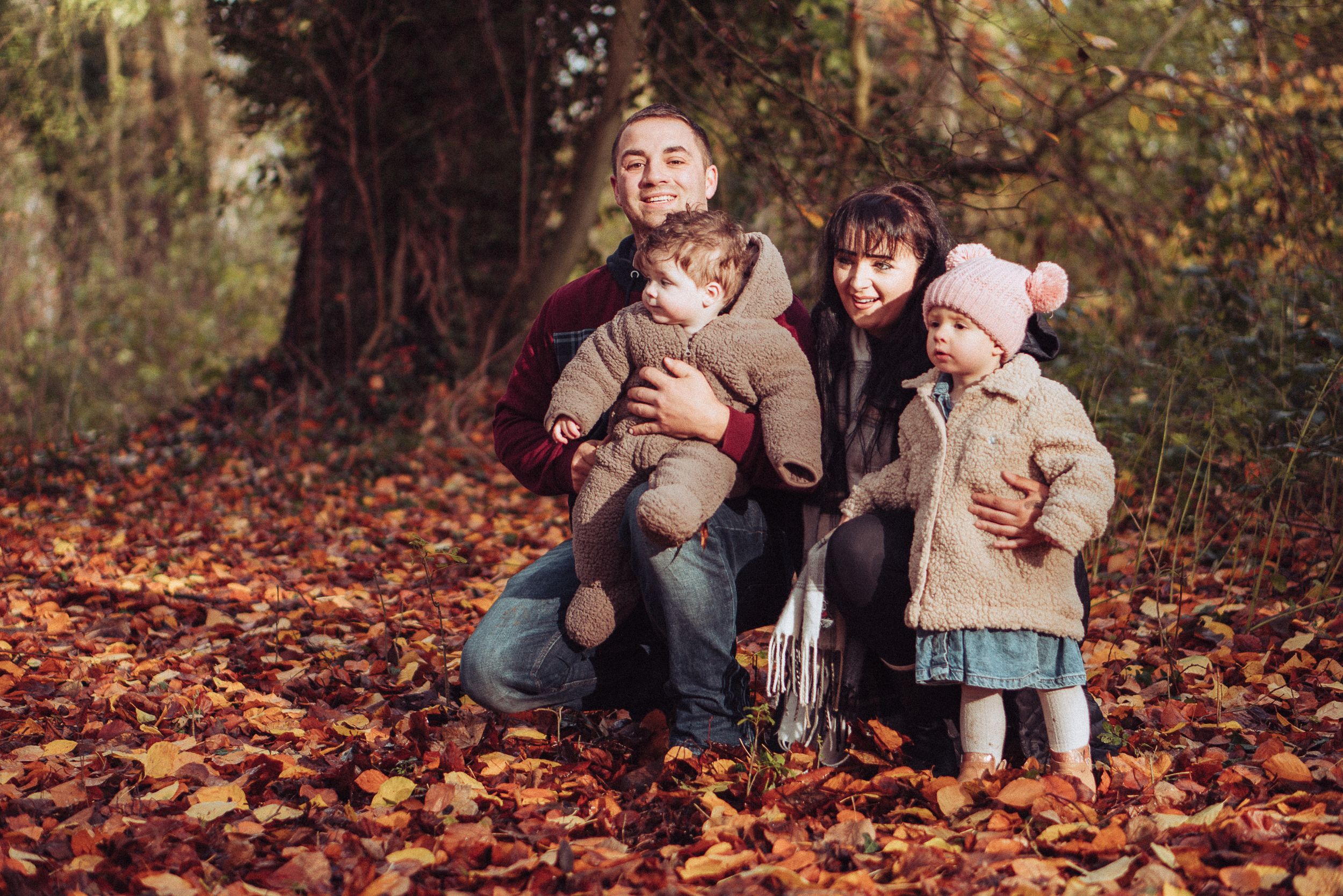 Young family crouched down in autumnal leaves, orange and brown