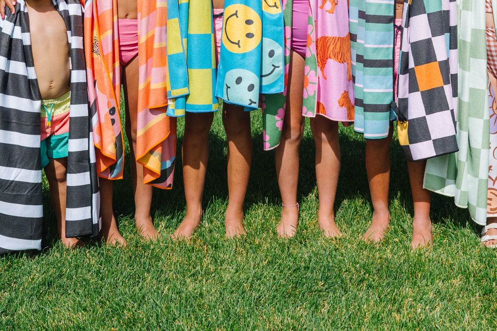Row of bare feet wearing colorful patterned towels standing on green grass.
