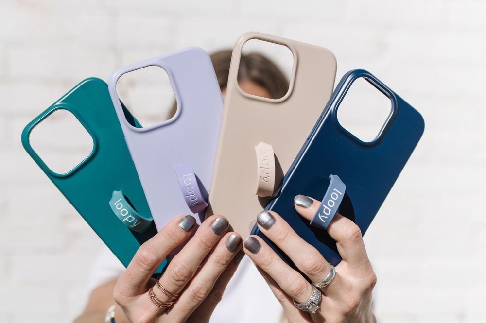 Four colorful iPhone cases in teal, lavender, beige and navy blue displayed in hands against white background.