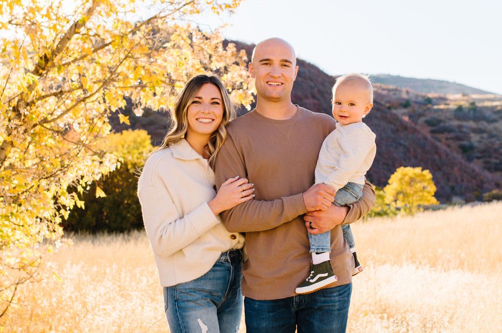 Family enjoying an autumn day outdoors with golden leaves and red rocks in the background.