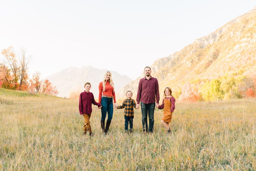 Family walking together through a golden field with mountains visible in background during sunset.