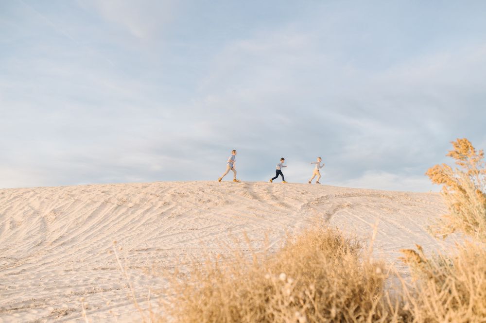 Three silhouettes walking along the ridge of a sand dune against a bright sky.