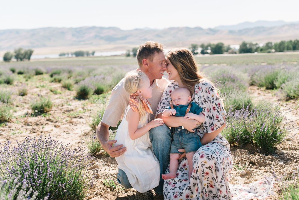 Family sits together in a blooming lavender field during golden hour in a rustic outdoor setting.