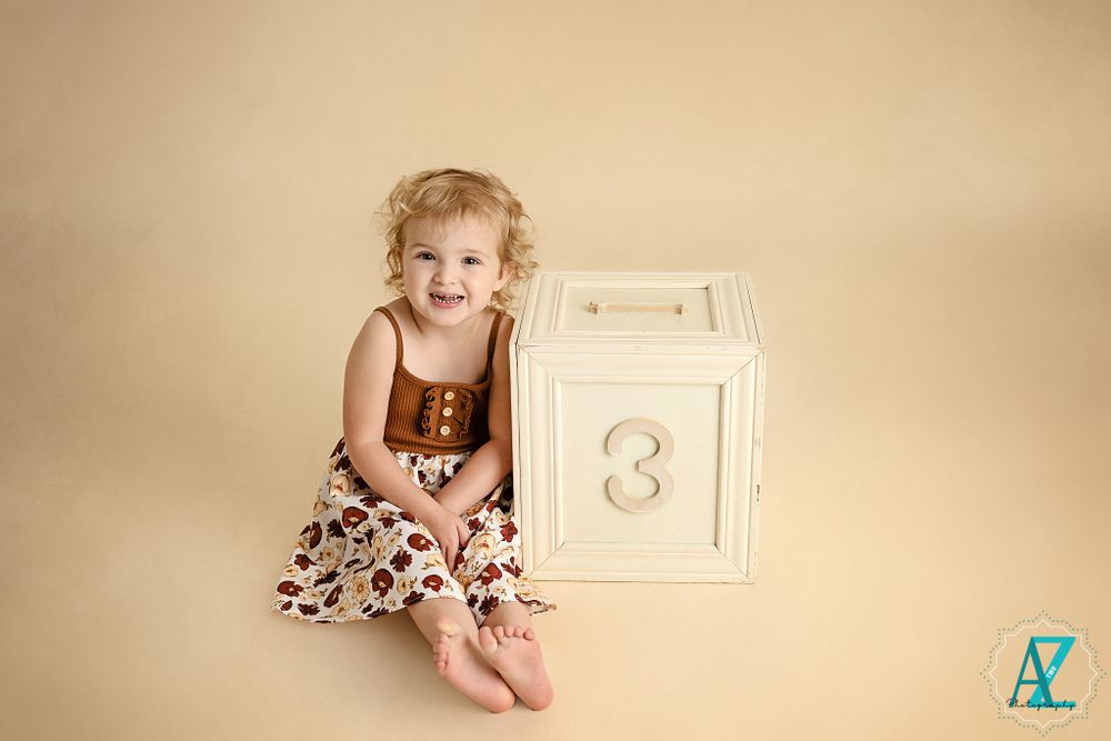 Happy child in brown and floral outfit poses on white decorative cube.