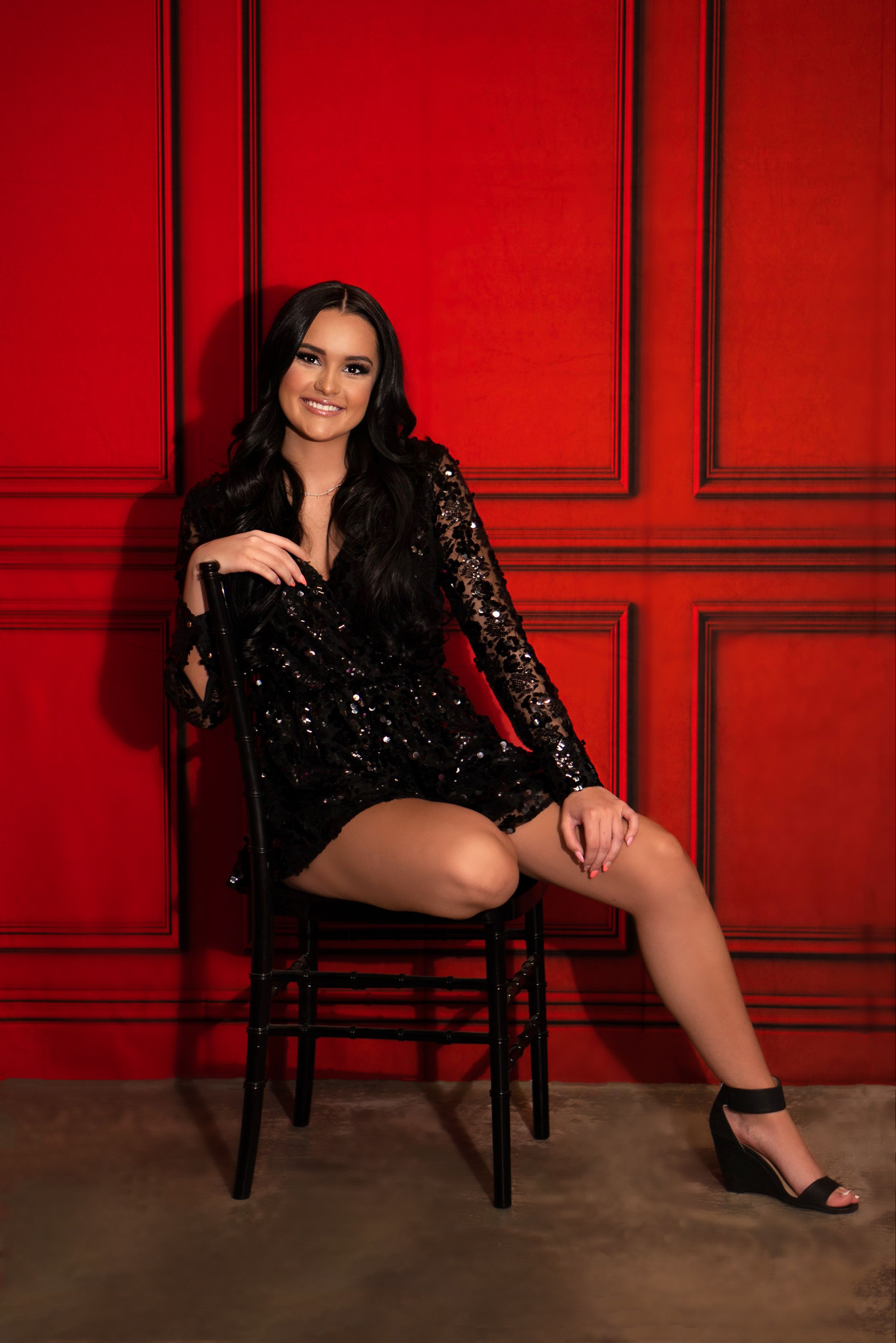 Glamour portrait session with sparkly black dress against red paneled wall.