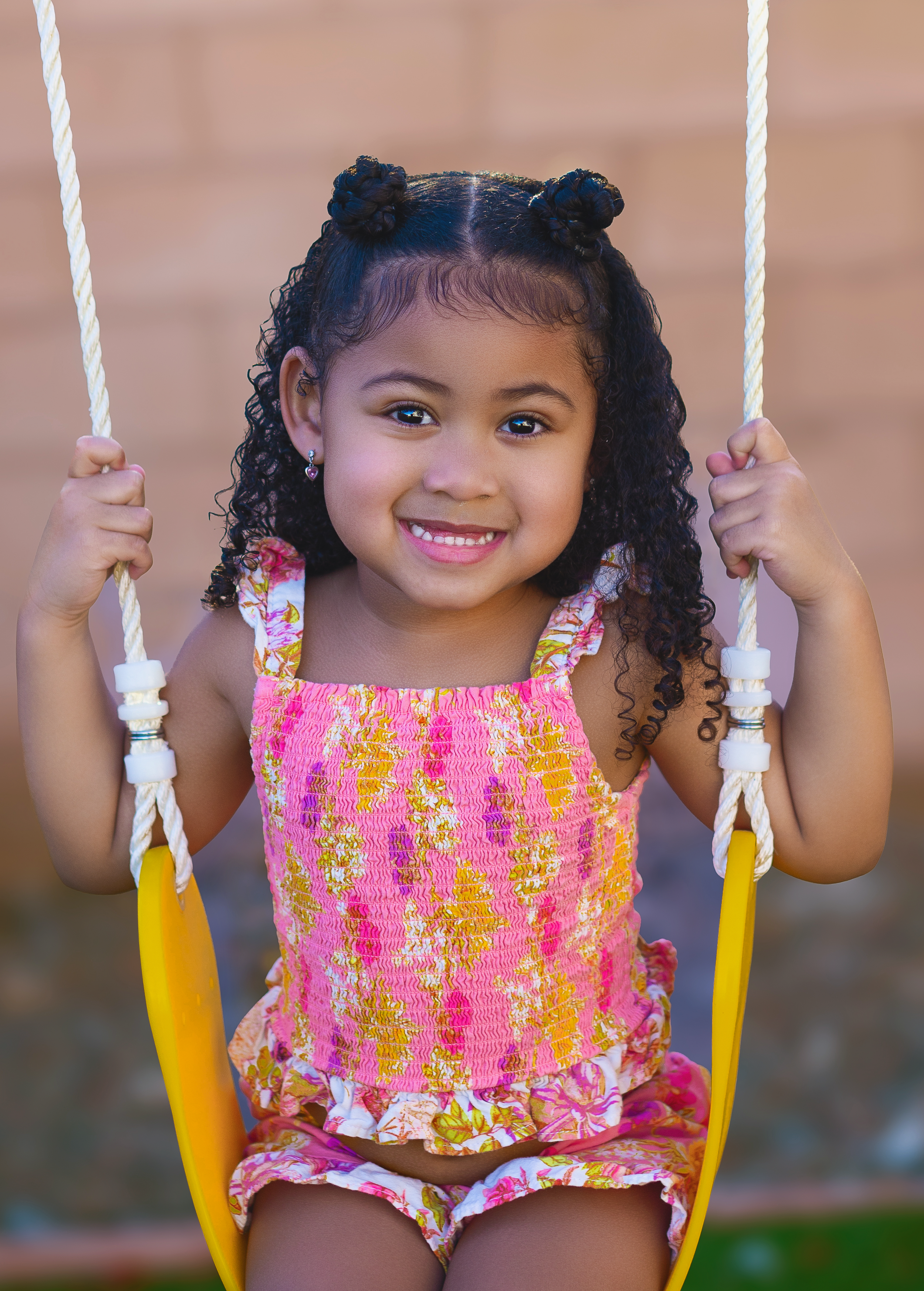 Child on yellow swing wearing bright pink floral outfit with joyful expression.