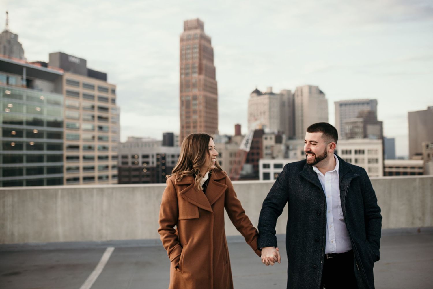 Couple walking hand in hand on urban rooftop with city skyline behind them.