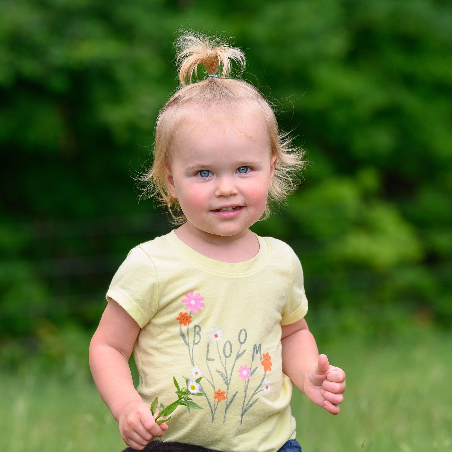 Toddler holding a flower wearing a shirt that says "Bloom"