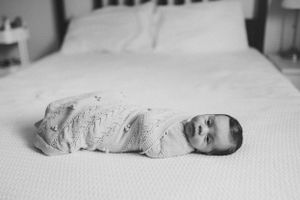 Black and white image of a swaddled newborn baby lying on a bed.