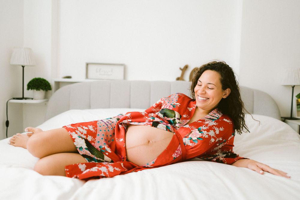 Maternity photo of woman in floral robe relaxing on white bed.