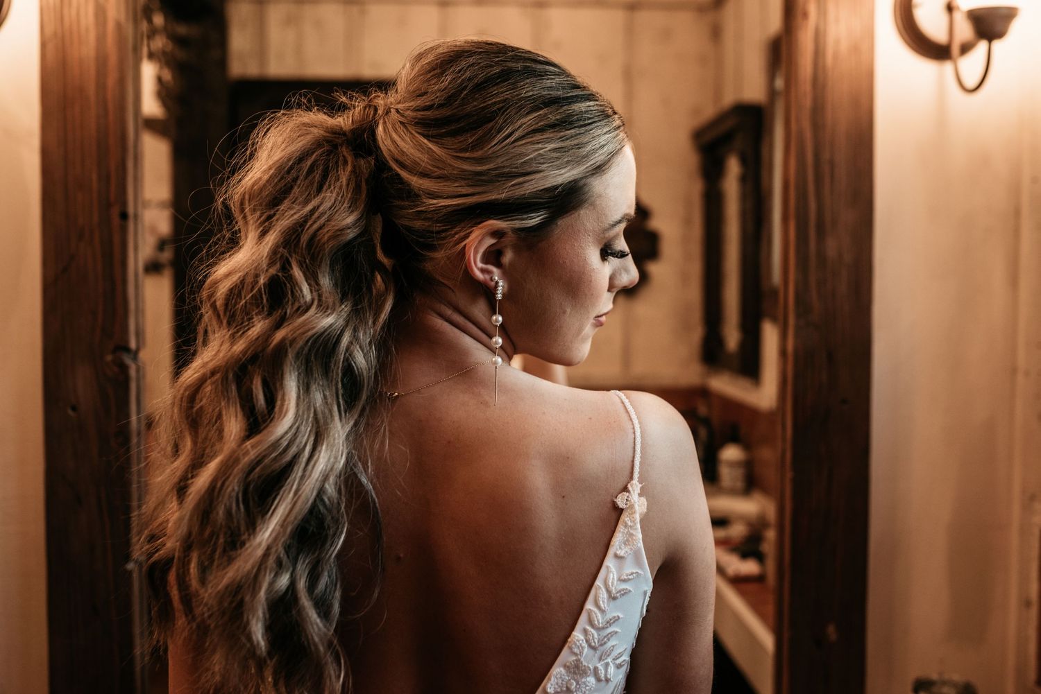Back view of an elegant bridal hairstyle with loose waves and a white dress strap.