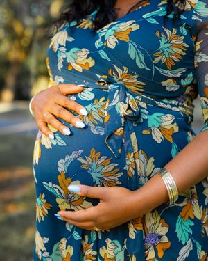 Close-up of hands cradling a pregnant belly in a blue floral dress.