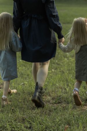A close-up view of legs walking through grass, showing denim dresses and boots.