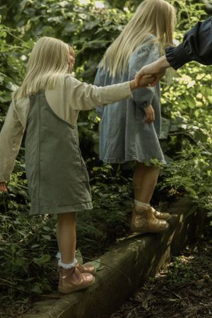 Children holding hands while walking on a fallen log in a wooded area.