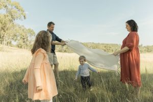 A family playing with picnic mat in a sunny field creating joyful movement.