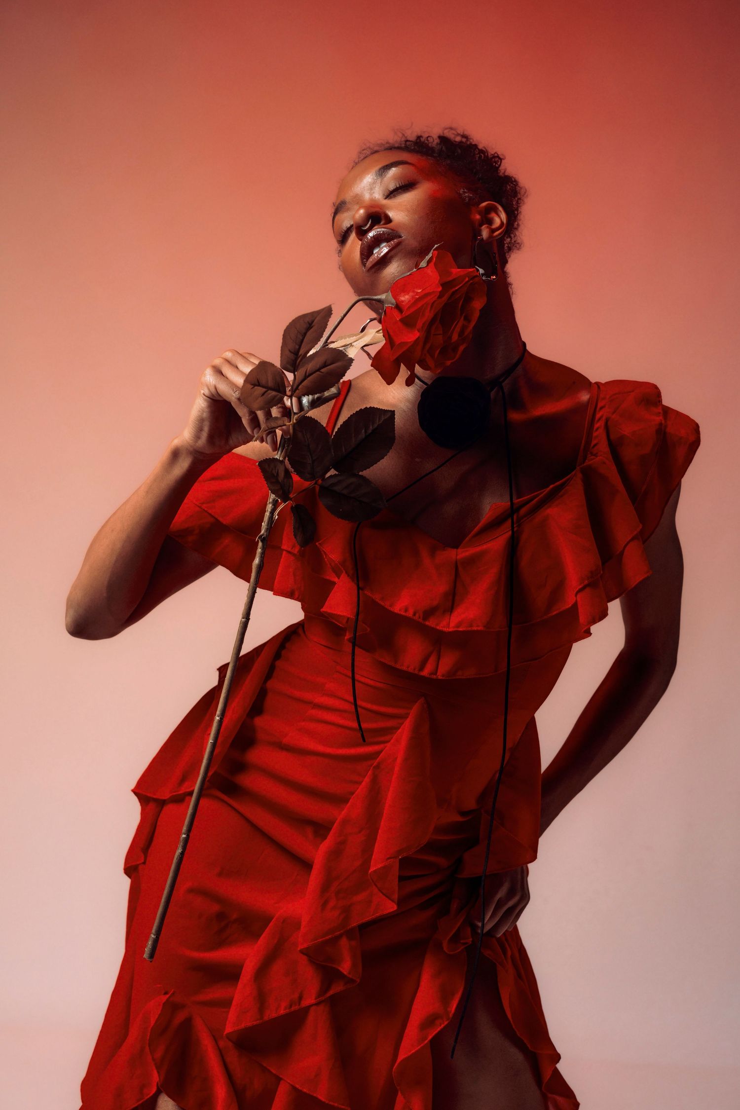 Artistic portrait in red dress against coral background with dramatic lighting.