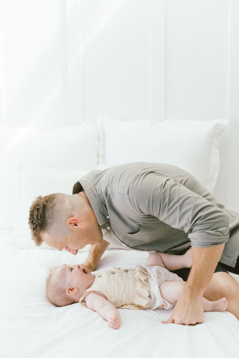 Adult leaning close to baby lying on white bedding.