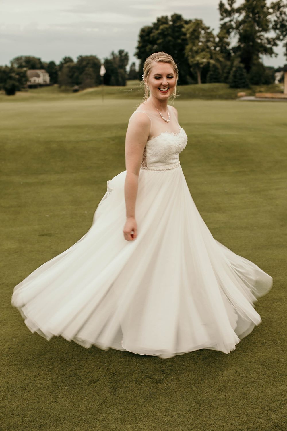 Bride in a flowing white strapless ball gown twirling on a lush green golf course.