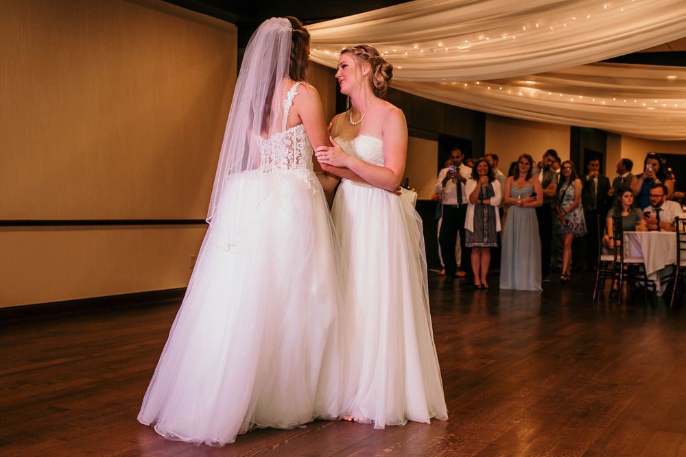 Two brides in white gowns share their first dance at wedding reception.