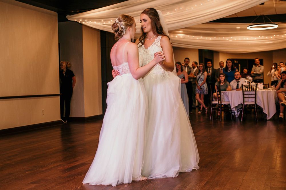 Two brides in elegant white gowns share an intimate first dance together.