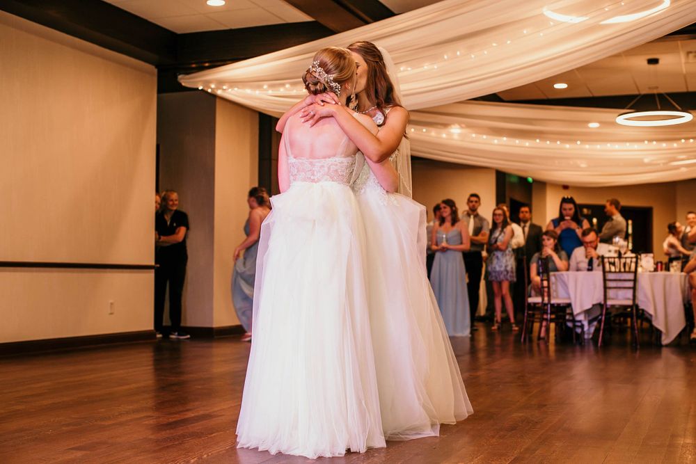 Two brides embrace warmly during their first dance at wedding reception.