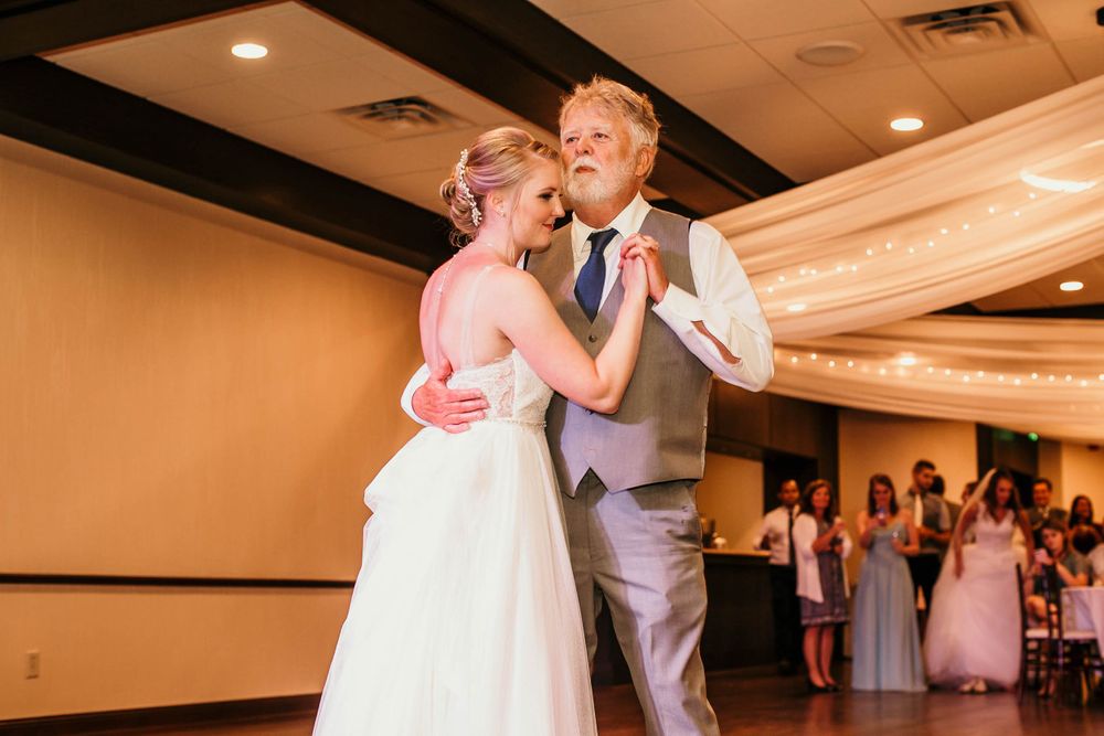 Bride in white gown shares father-daughter dance at wedding reception.