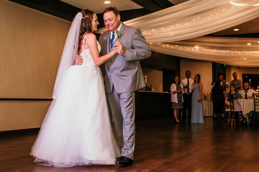 Bride in veil and father in gray suit share father-daughter wedding dance.