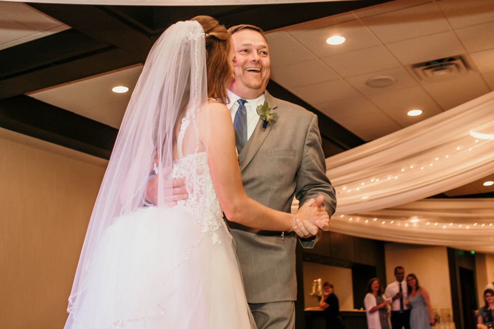 Smiling father in gray suit dances joyfully with bride at wedding reception.