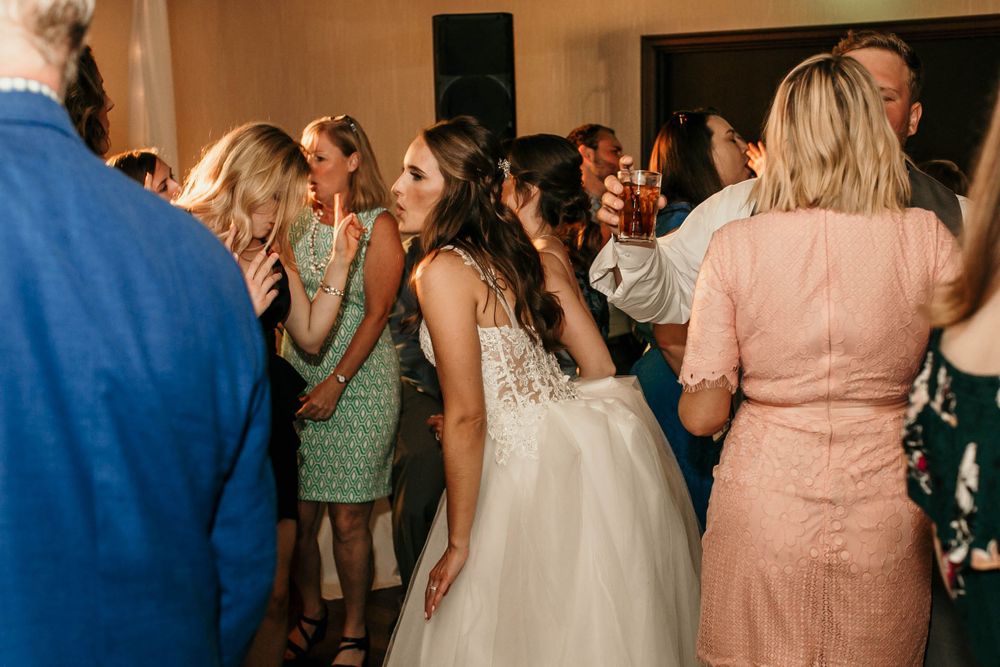 Bride in lace wedding gown mingles with guests on crowded wedding reception dance floor.