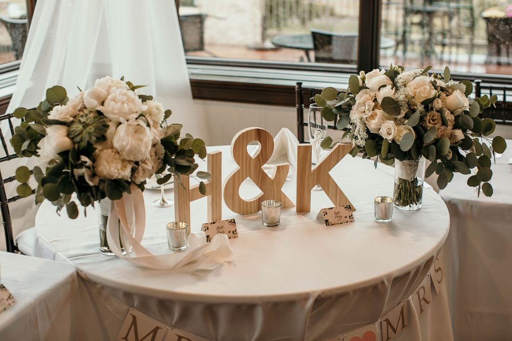 Wedding sweetheart table with H&K wooden letters, white floral bouquets, and Mrs. & Mrs. banner.
