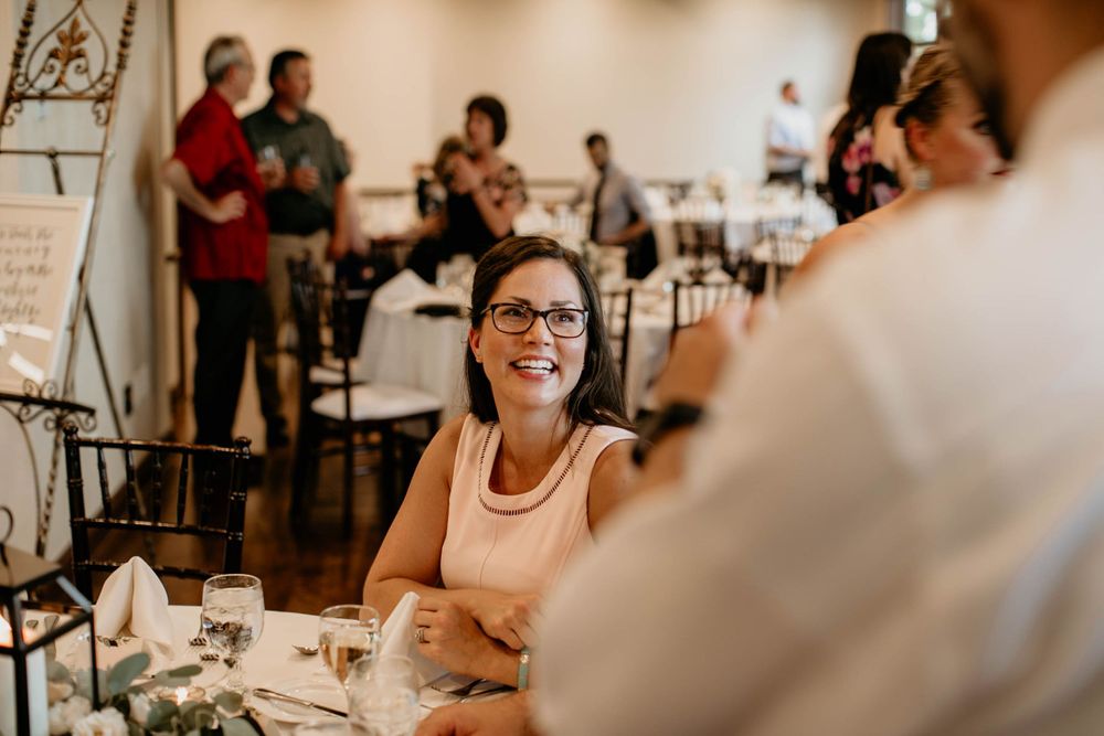 Smiling woman with glasses enjoys a wedding reception dinner at an elegantly decorated table.