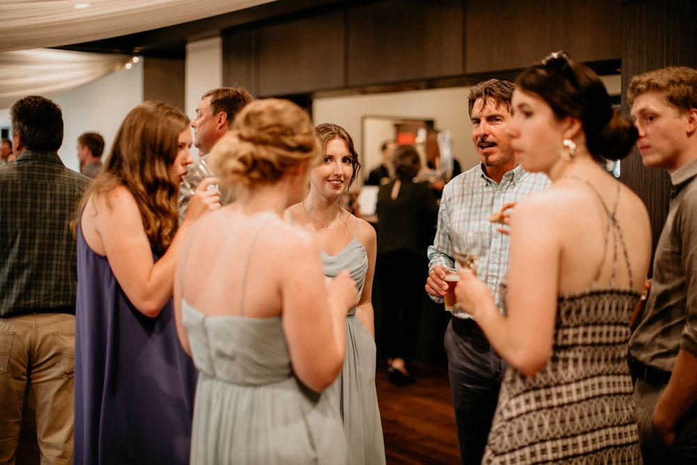 Bride in white gown laughing with guests holding champagne at wedding reception.
