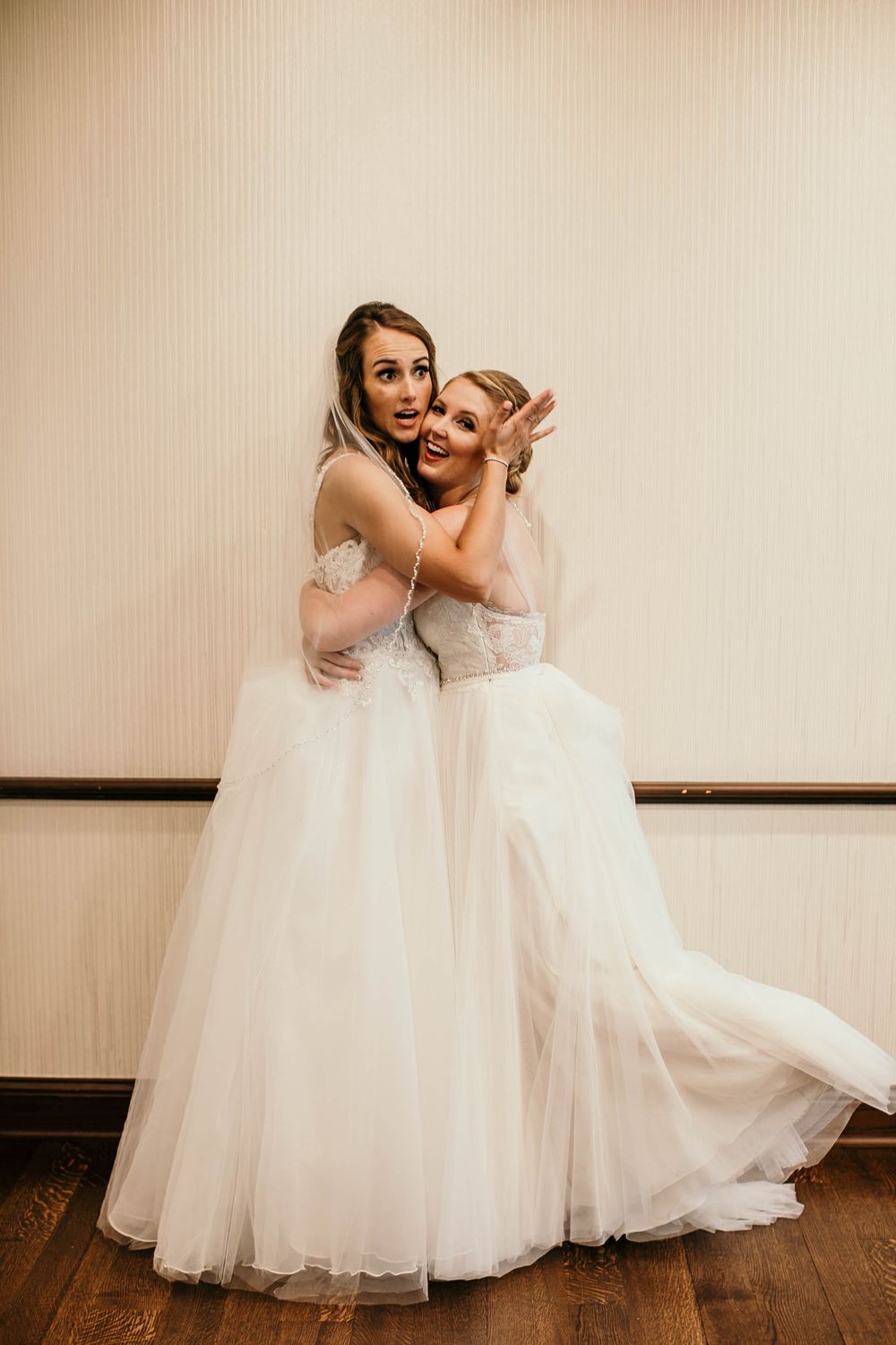 Bride in white lace gown posing with smiling guest near dessert table at reception.