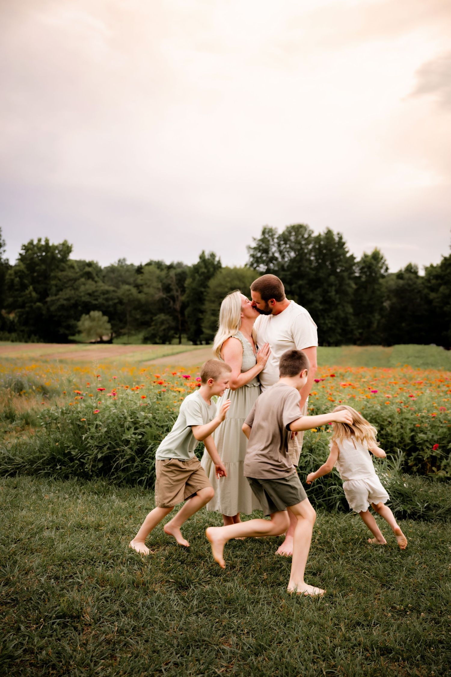 A family shares a tender moment in a vibrant flower field, as children run toward their embracing parents at sunset.