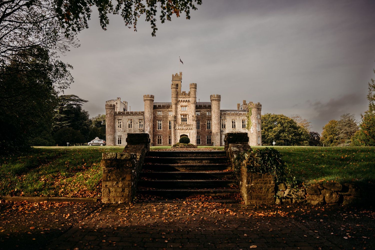 Majestic castle on hilltop with stone steps and autumn leaves in foreground.