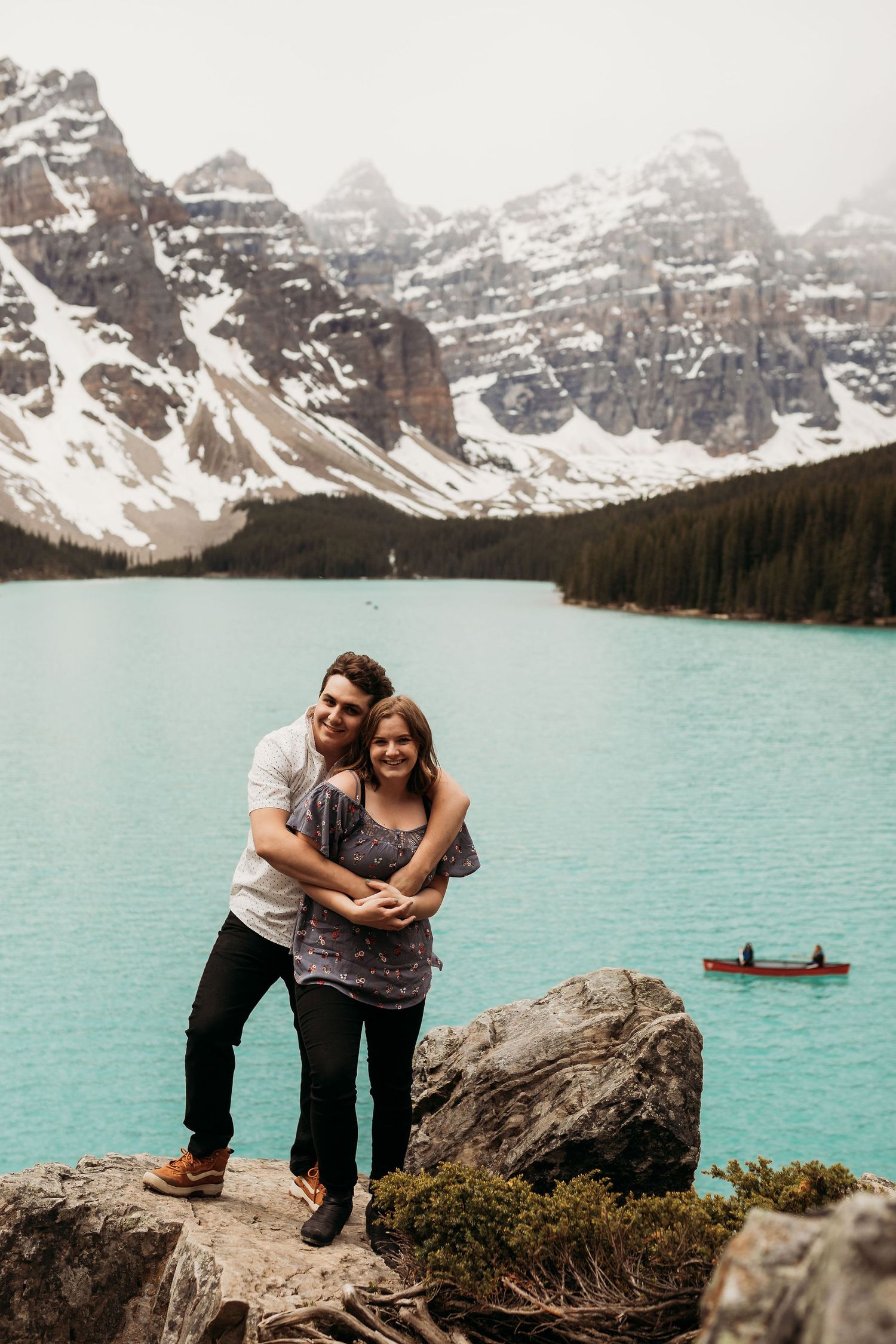 Couple posing on rocky overlook at Moraine Lake with turquoise waters and mountain vista.