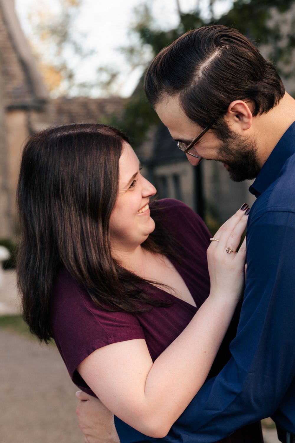 A couple shares an intimate moment outdoors, with her in a purple top and him wearing a navy blue shirt and glasses.
