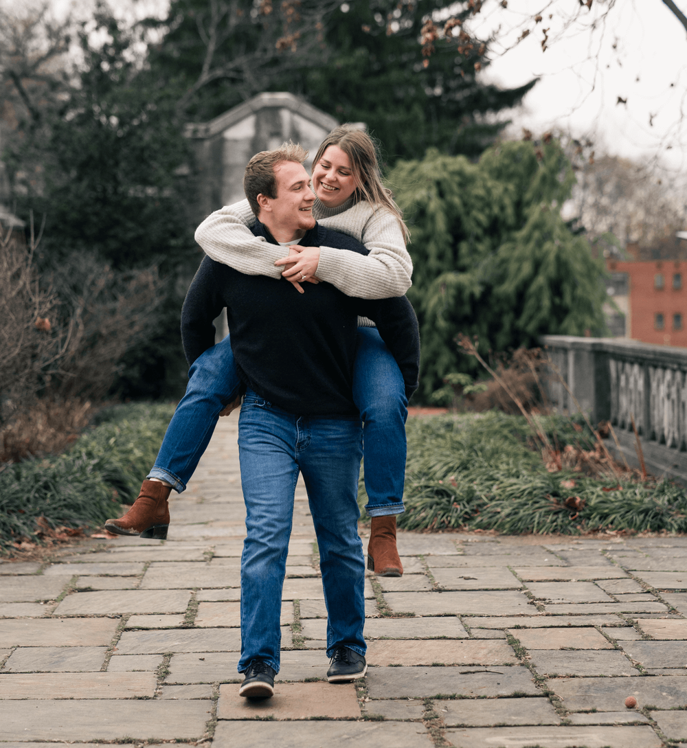 A couple embraces and dances together on a stone pathway surrounded by greenery and trees.