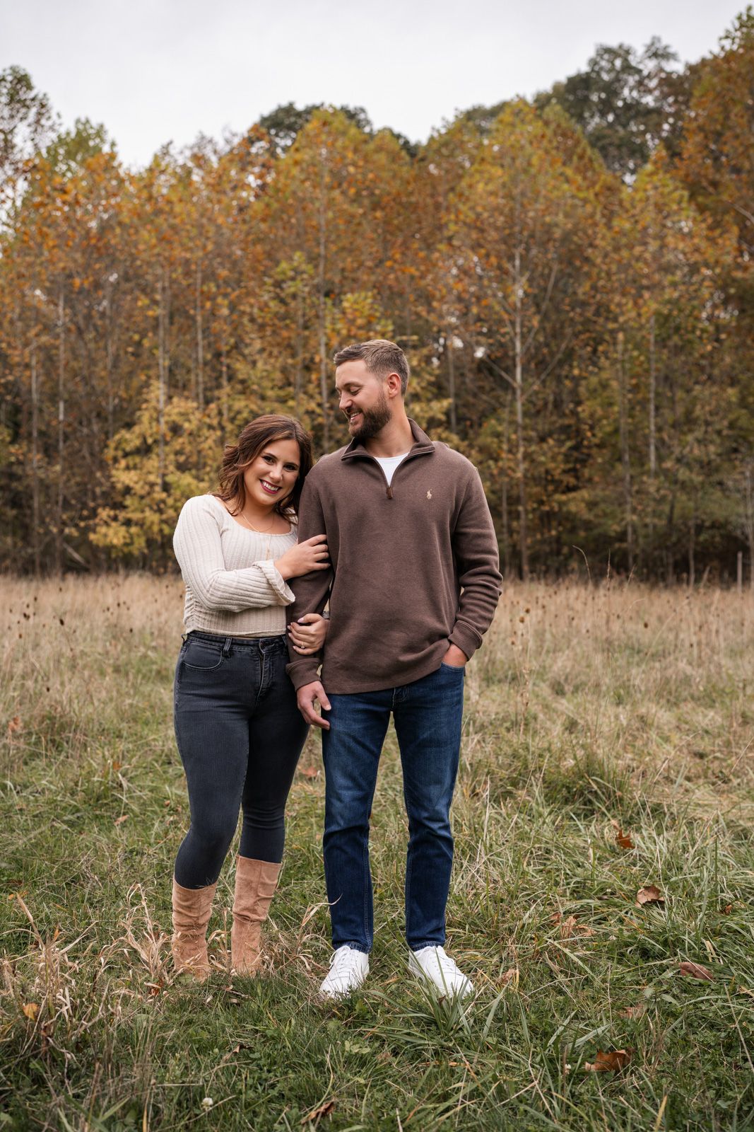 A couple shares a tender moment while walking through an autumn field with golden trees in the background.